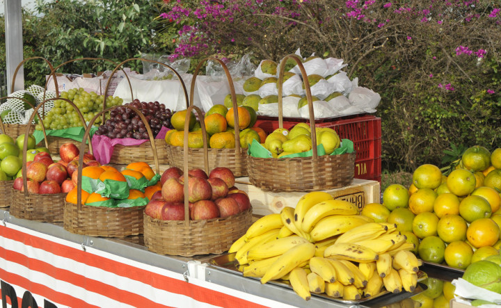 Imagem mostra banca com diversas frutas como banana, maça, laranja, entre outras, em cestas. 