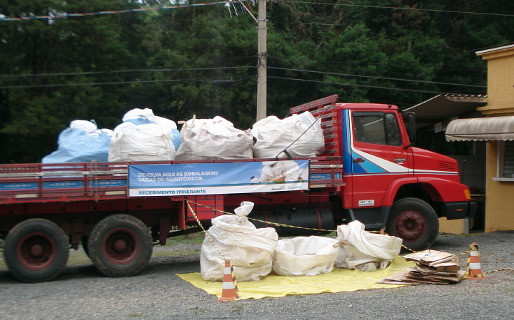 Imagem mostra caminhão vermelho, com grandes embalagens plásticas na carrorceria.