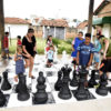 Crianças e pais brincam em xadrez gigante