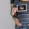 Mulher grávida segura foto de ultrassom com um homem atrás segurando sua barriga