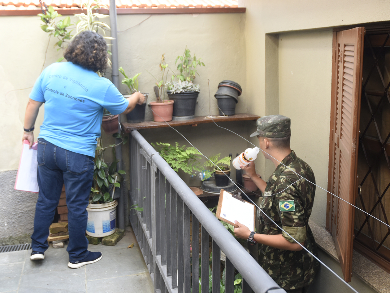Moradora mostra vaso enquanto militar verifica um frasco