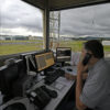 Técnico em atendimento na torre de controle do aeroporto com visão da pista e equipamentos de monitoramento de aviões
