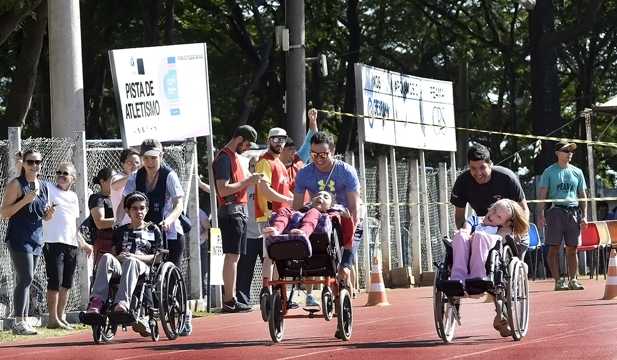 Três pessoas empurrar três cadeirantes na pista de atletismo do Bolão