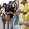 Pessoas com camiseta amarela distribuem laços para pedestres, com o mascote Farolito atrás