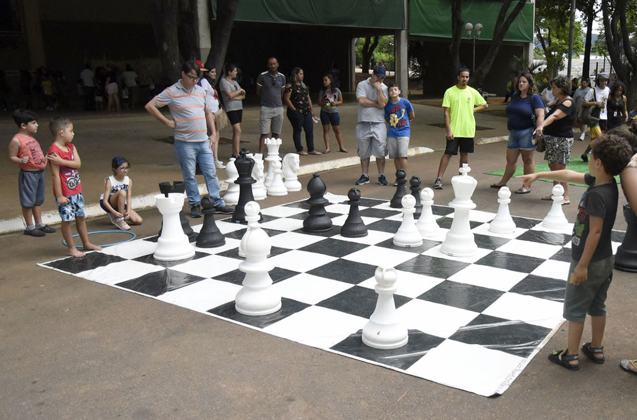 Crianças e adultos jogam xadrez em tabuleiro com tamanho humano