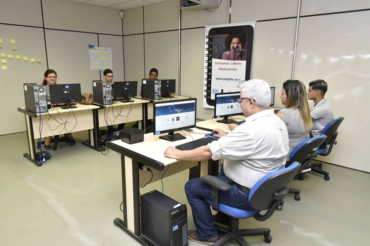 Seis pessoas usando computador, em duas fileiras, uma de frente com a outra
