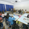 Jovens reunidos em círculo, sentados em carteiros, dentro de uma sala de aula
