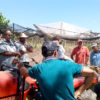 Agricultores conversam em roda com plantação ao fundo