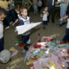 Crianças com uniformes da rede municipal agrupam aviões de papel no térreo do Paço Municipal