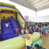 Brinquedo inflável, com crianças pulando e em fila, em quadra coberta