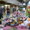 Foto com primeiro plano em bonecas e artesanato de pano colorido e pessoas passando ao lado