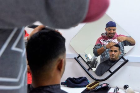 Homem corta o cabelo de outro em frente ao espelho