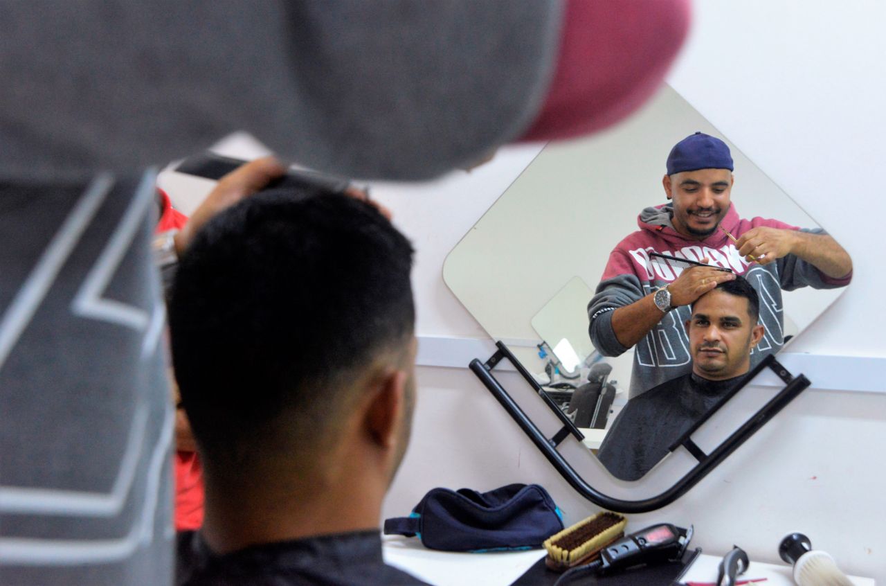 Homem corta o cabelo de outro em frente ao espelho