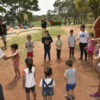 Crianças em brincadeira com bola de pingue pongue em gramado do parque, com monitores