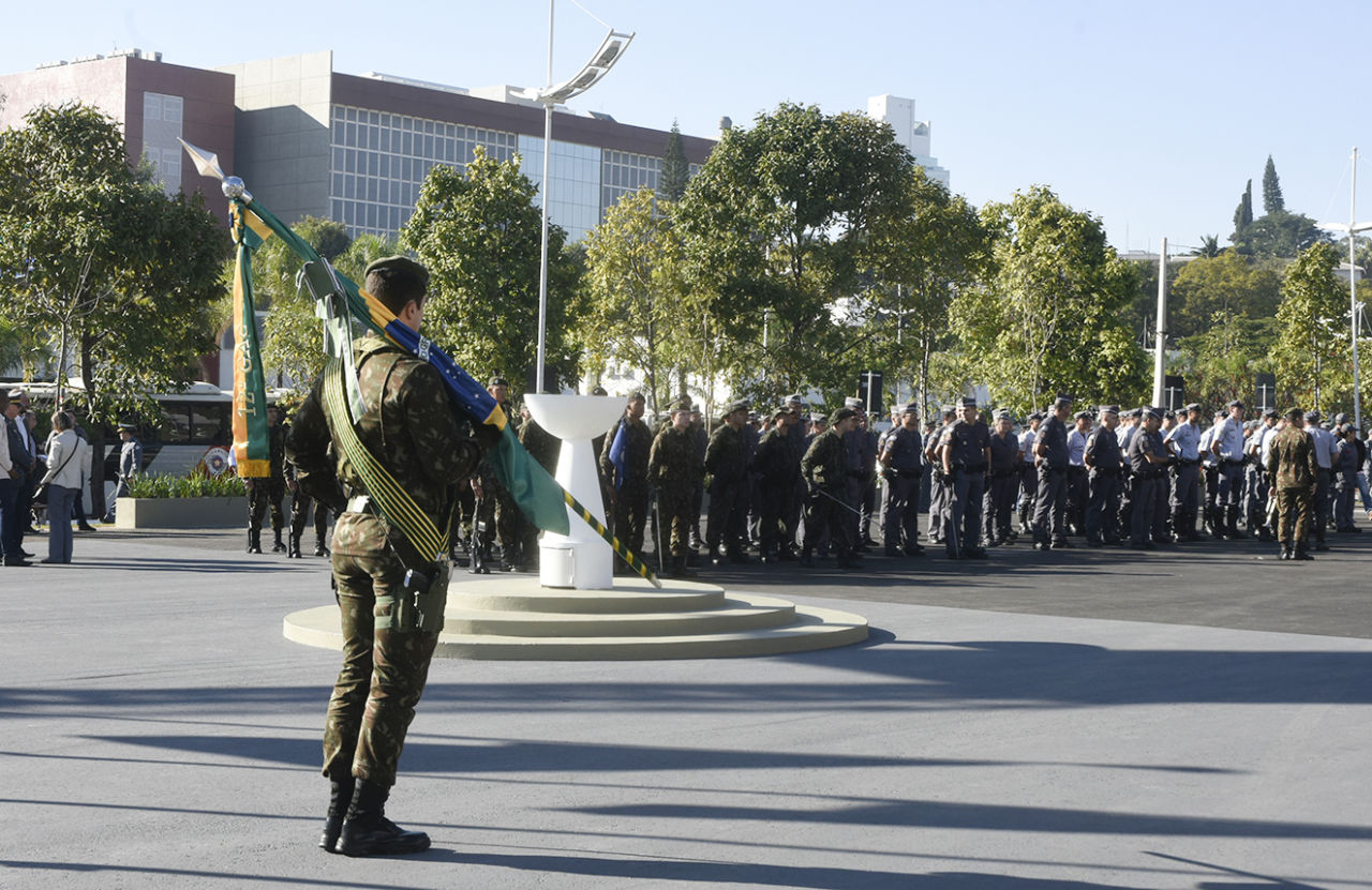 Militar segura bandeira do Brasil enquanto outros militares perfilados observam