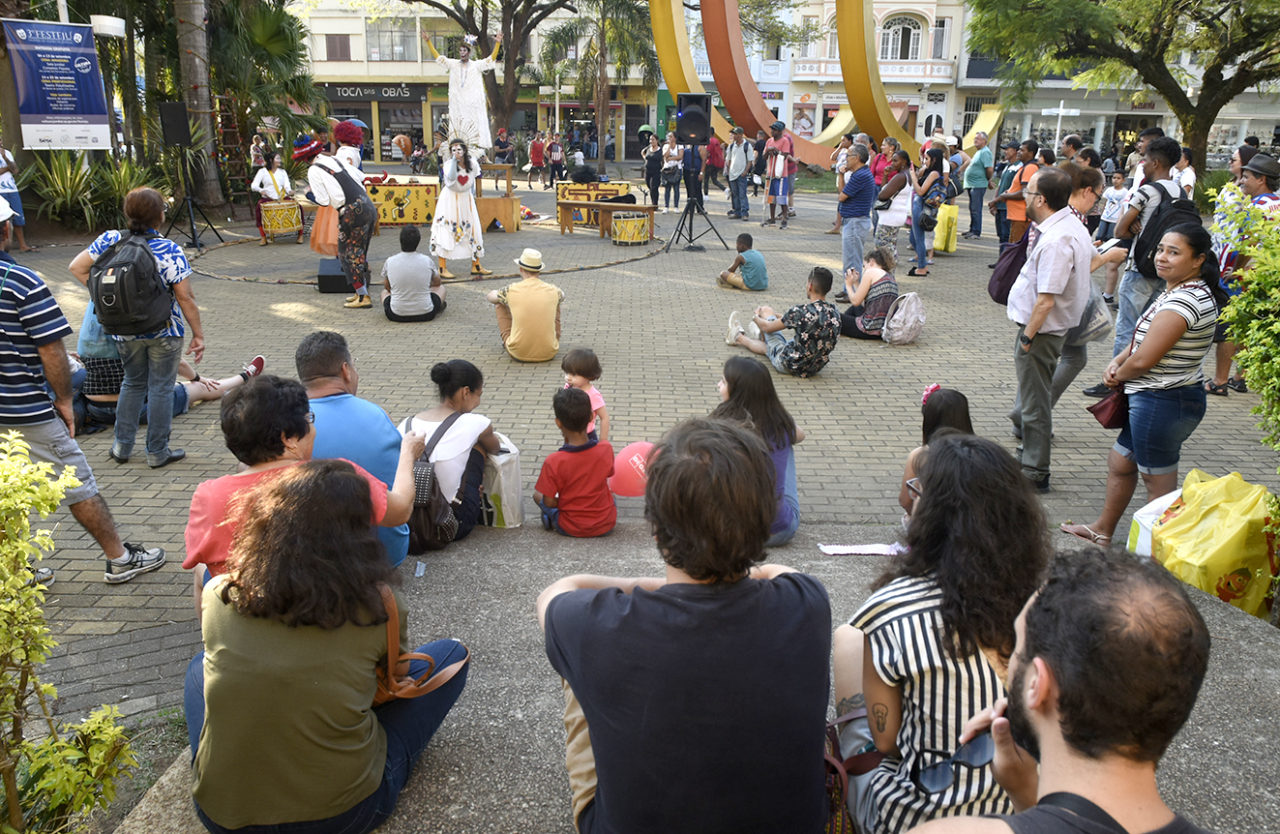 Pessoas sentadas no chão em uma praça, em torno de um palco improvisado