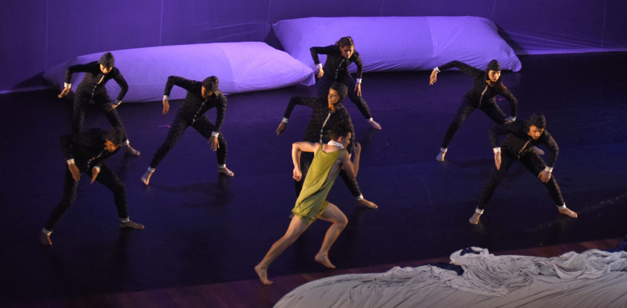 Bailarinos em performance sobre palco, com dois travesseiros gigantes