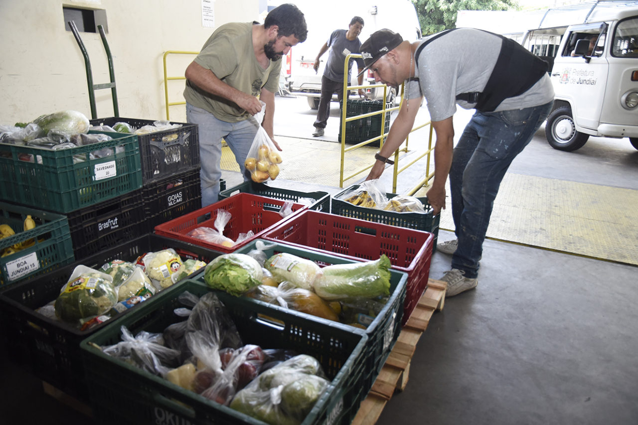 Homens carregam caixas com frutas, verduras e legumes 