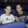 Foto posada de menina ao lado a mãe, sentadas em plateia de teatro
