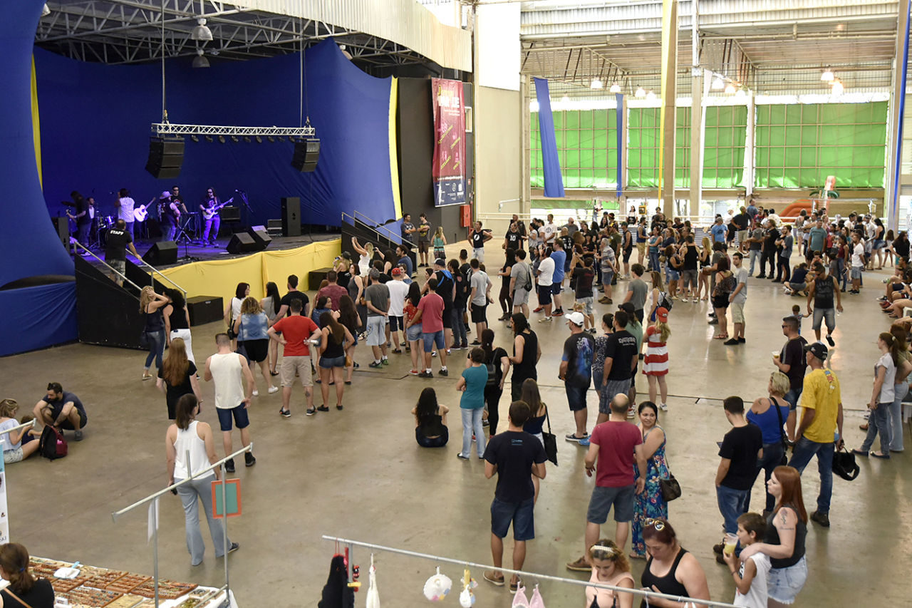 Pavilhão coberto, com pessoas em pé assistindo a show em palco