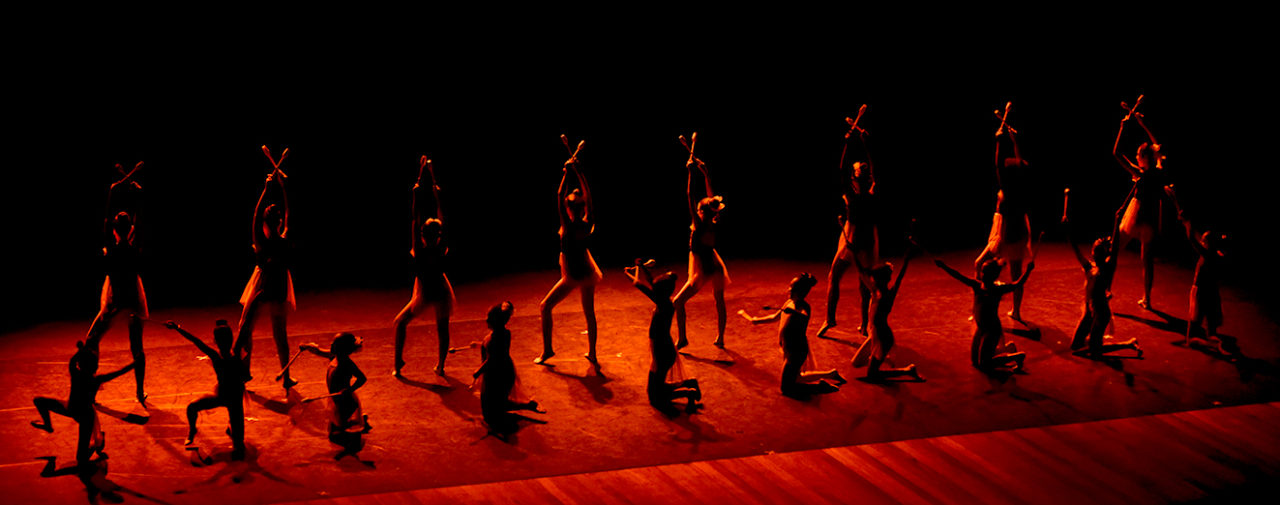 Atletas se apresentando em palco escuro, iluminado com luz vermelha