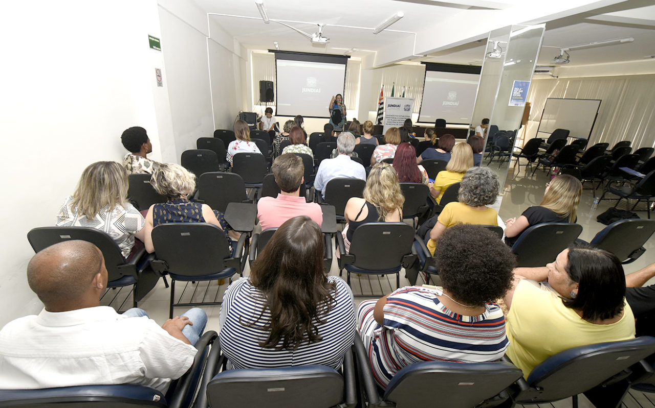 Foto de costas de pessoas sentadas em auditório, assistindo a uma apresentação