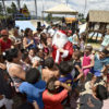 Homem fantasiado de Papai Noel interagindo com crianças em seu entorno