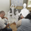 Pessoas de costas, sentadas, montando peças de artesanato em papel