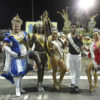 Personagens carnavalescos com fantasias, em foto posada em meio a uma avenida de desfiles