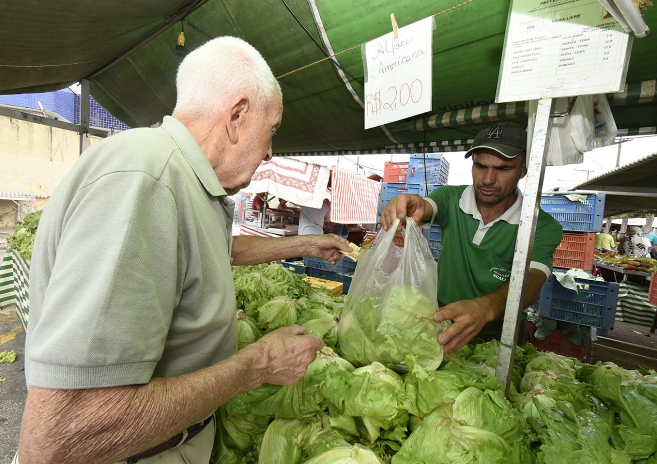 Homem recebe verduras em banca da feira