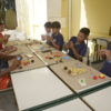 Crianças sentadas dos dois lados de mesas, brincando com massinha de modelar coloridas