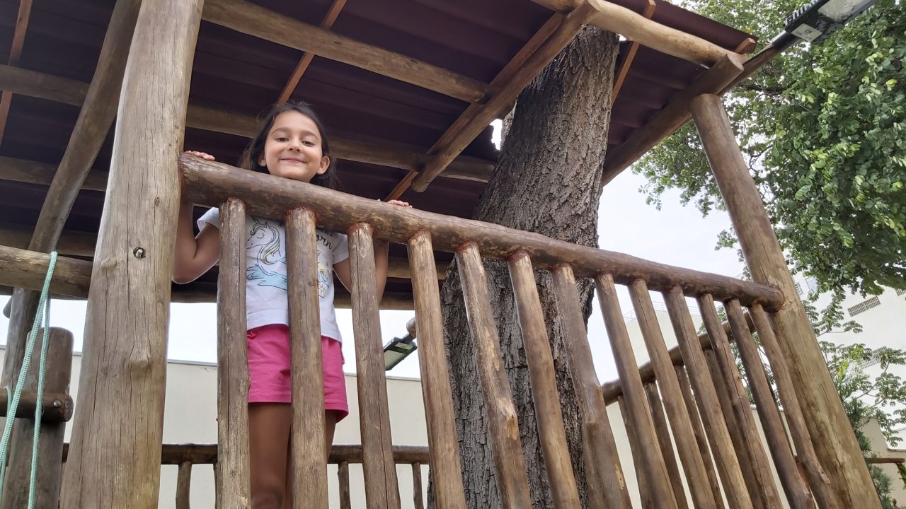 Foto posada de menina apoiada em saca de madeira de casa na árvore