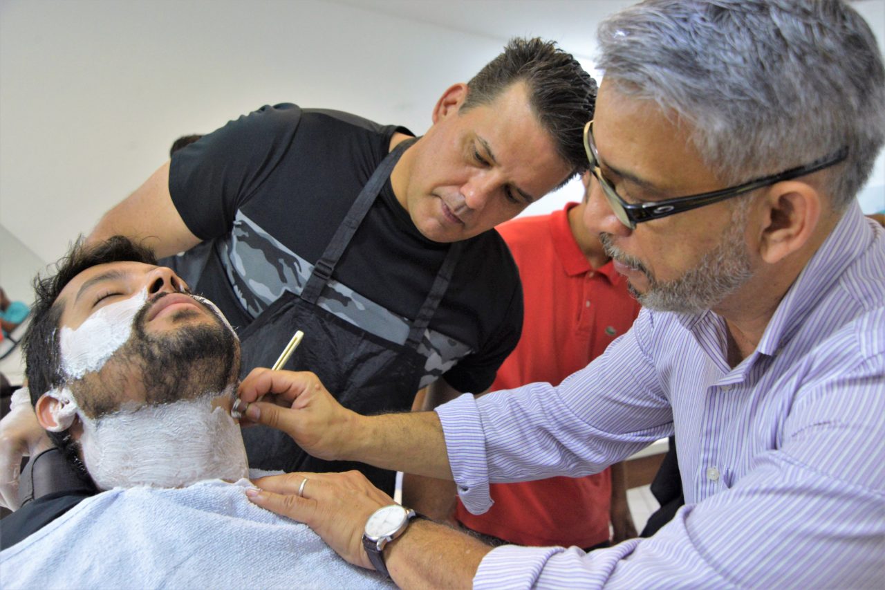 Professor ensinando dois alunos no curso de barbearia em atividade prática