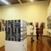 Sala de exposições, com homem, mulher e criança olhando para quadros abstratos e conversando