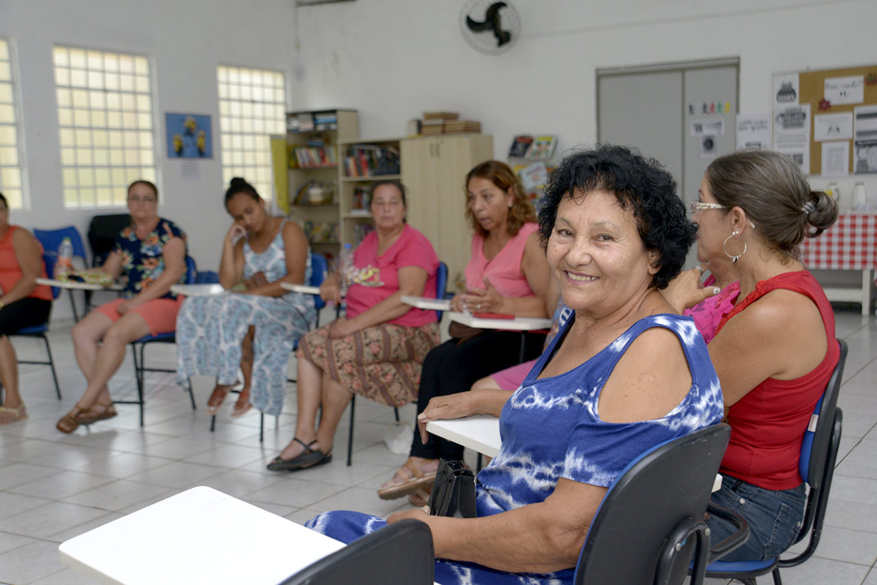 Mulheres sentadas em círculo, conversando, com uma mulher posando sorridente 
