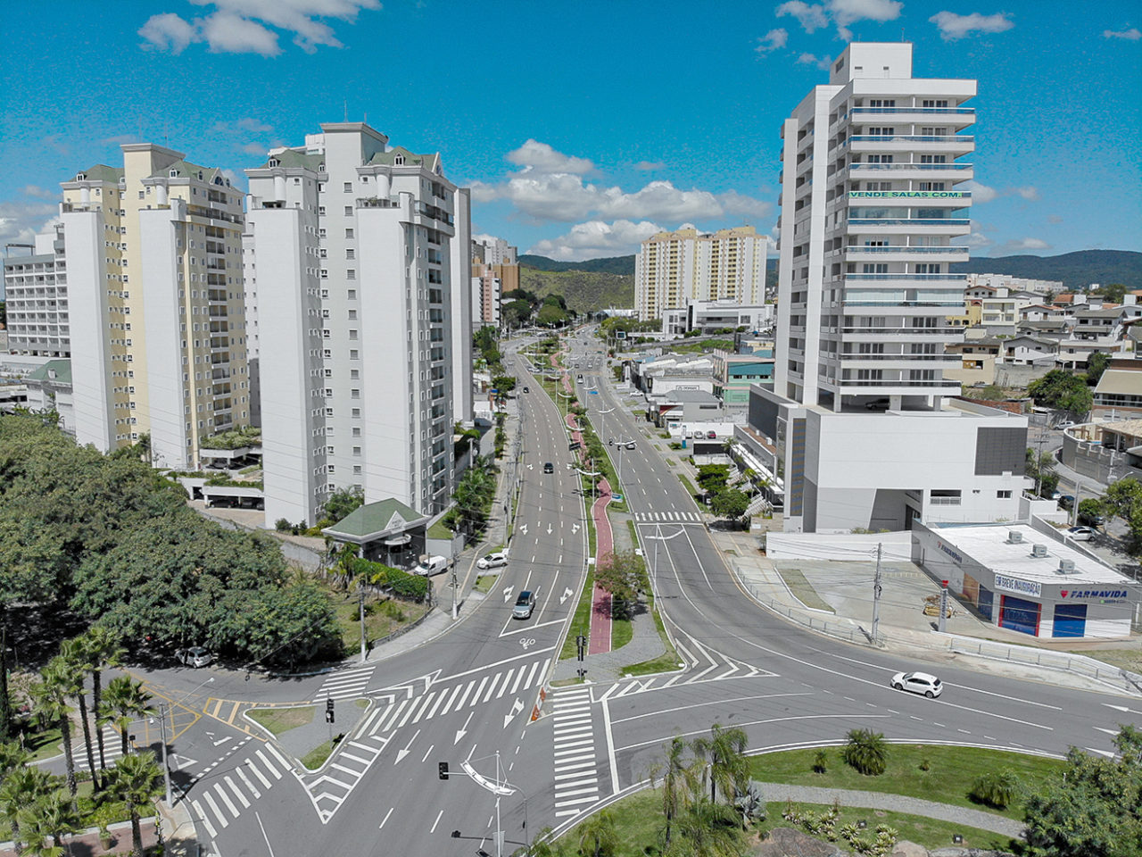 Foto aérea de avenida com pistas largas, prédios ao redor e uma praça central