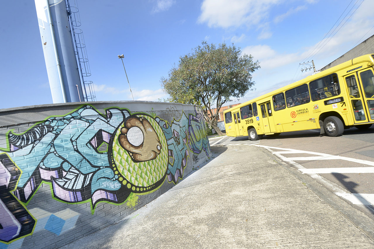 Ônibus passando na rua, com torre e parede grafitada ao lado