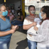 Servidora da Saúde entrega máscara de tecido e folheto explicativo sobre a COVID-19 a passageiras