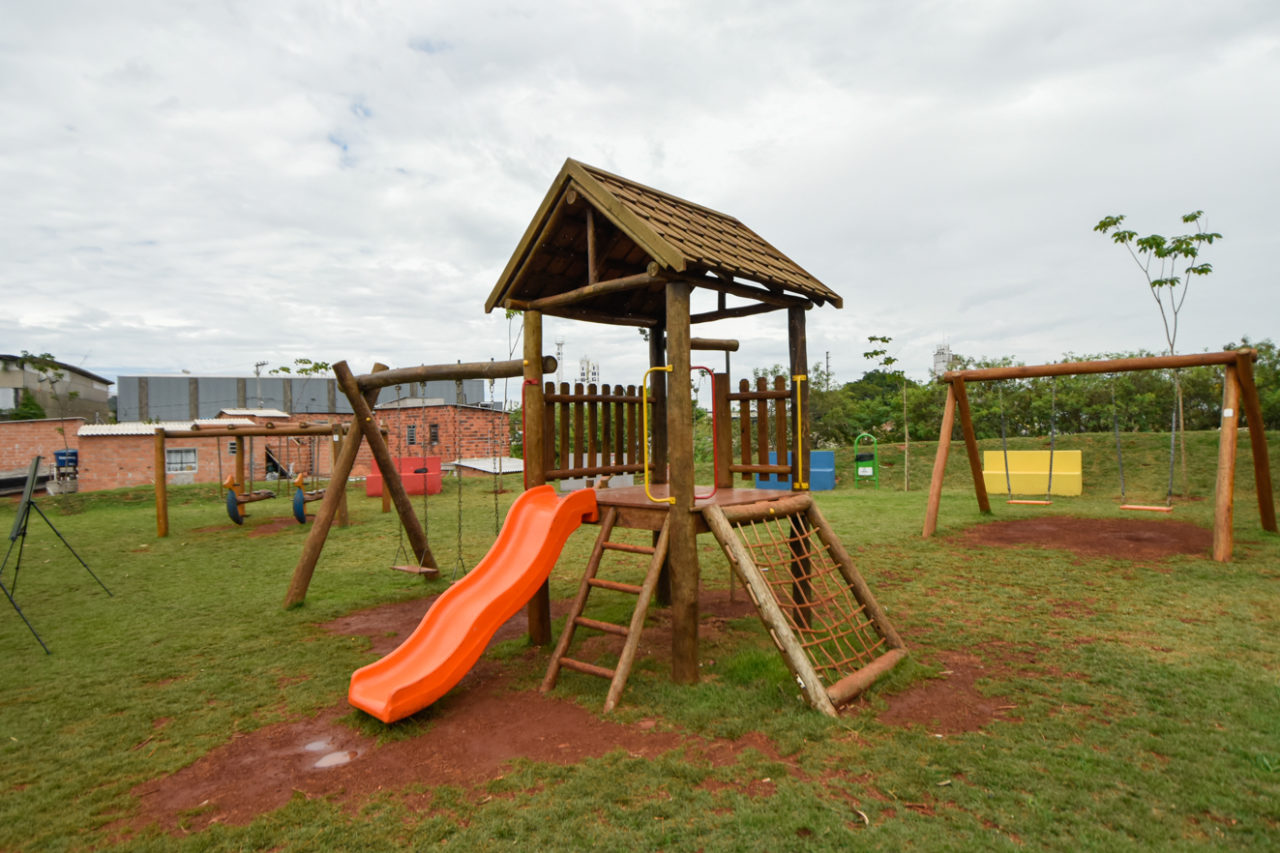 Parque infantil em gramado com balanças, escorregador, casinha de madeira e outros brinquedos