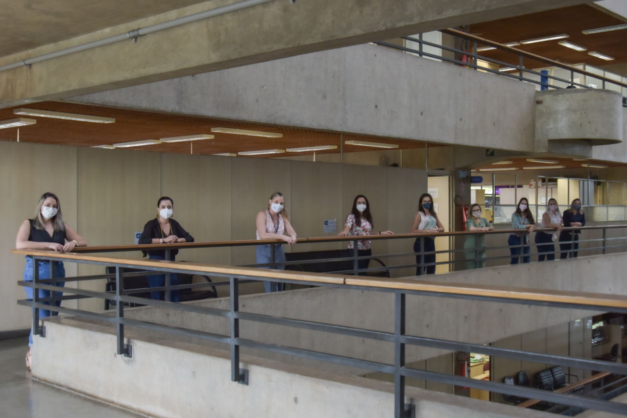 Nove mulheres usando máscaras apoiadas em corredor de prédio.