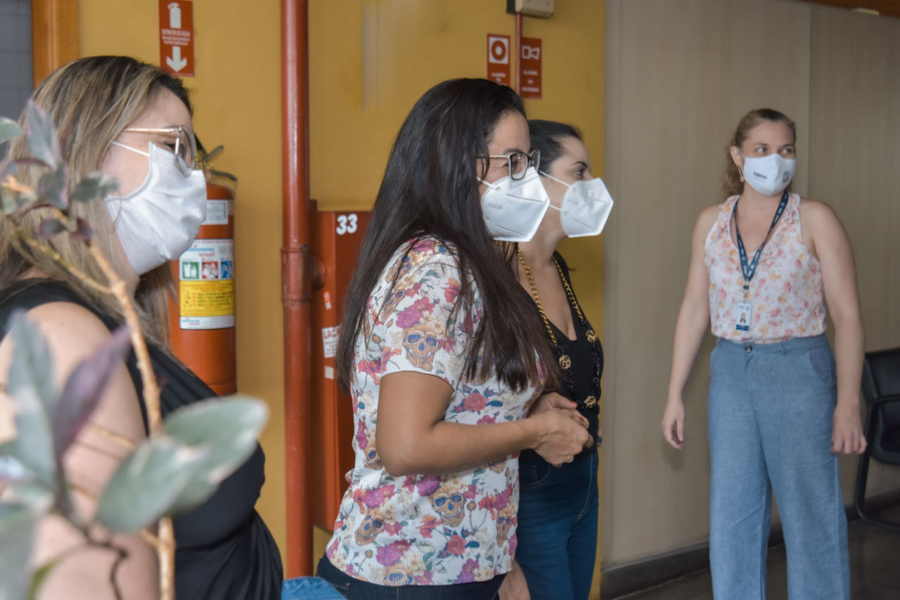 Quatro mulheres usando máscaras, em corredor de prédio com extintores de incêndio ao fundo