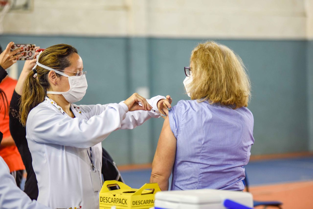 Enfermeira aplica vacina no braço esquerdo de mulher.