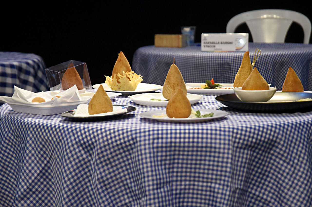 Imagem mostra mesa, com nove coxinhas em cima de pratos individuais