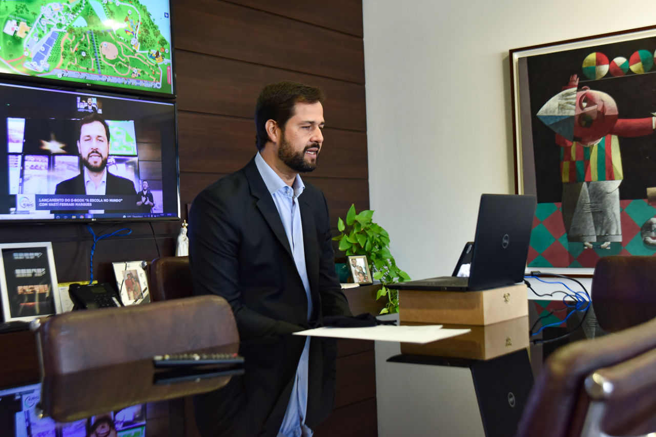 Imagem mostra homem (prefeito Luiz Fernando), em frente notebook, no fundo televisão transmitindo a live em que ele está presente.