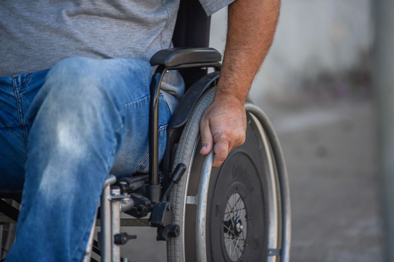 Imagem mostra homem em cadeira de rodas. detalhe está nas mãos e rodas.