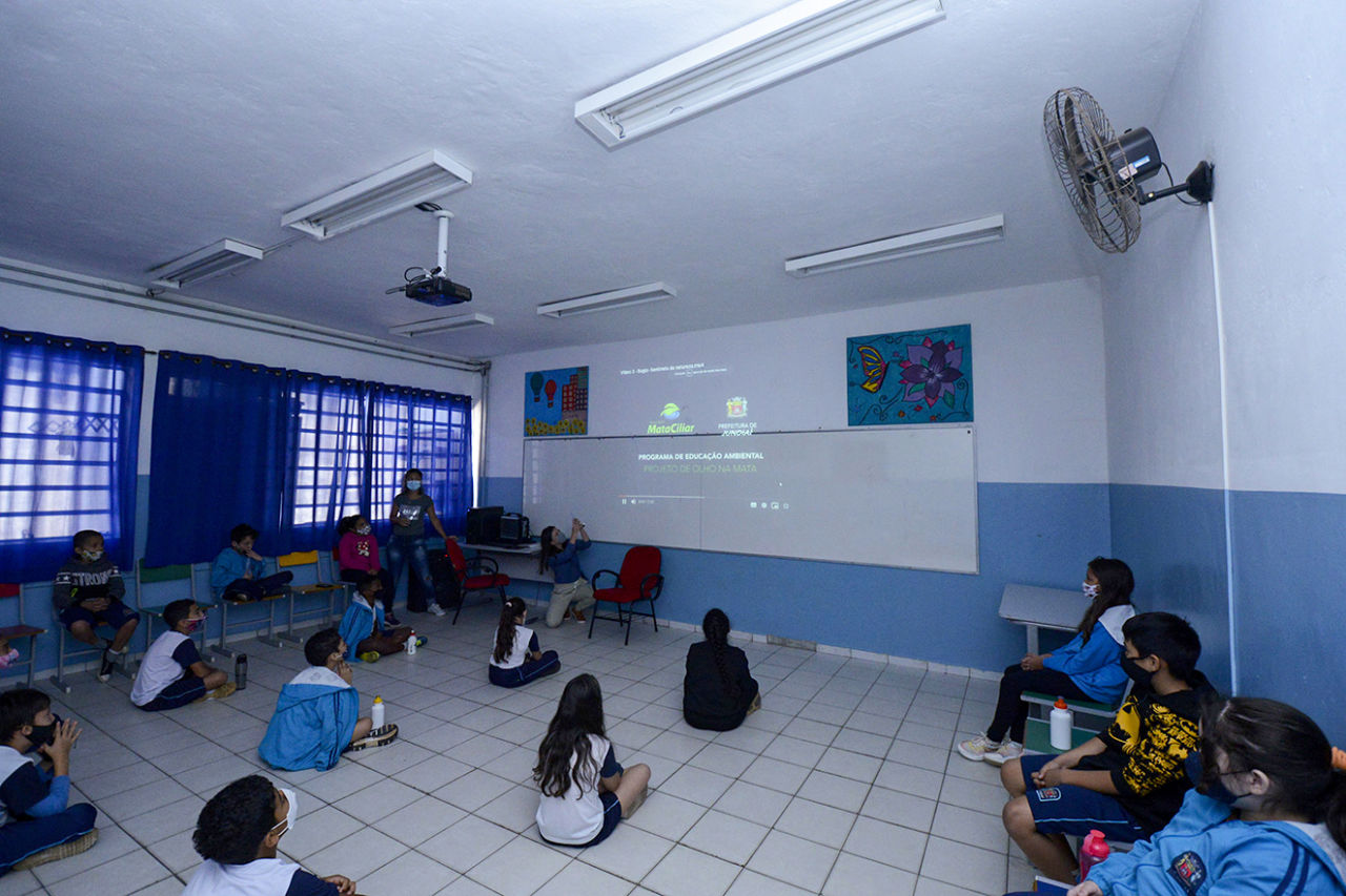 Imagem mostra sala de aula com crianças assistindo a vídeo 