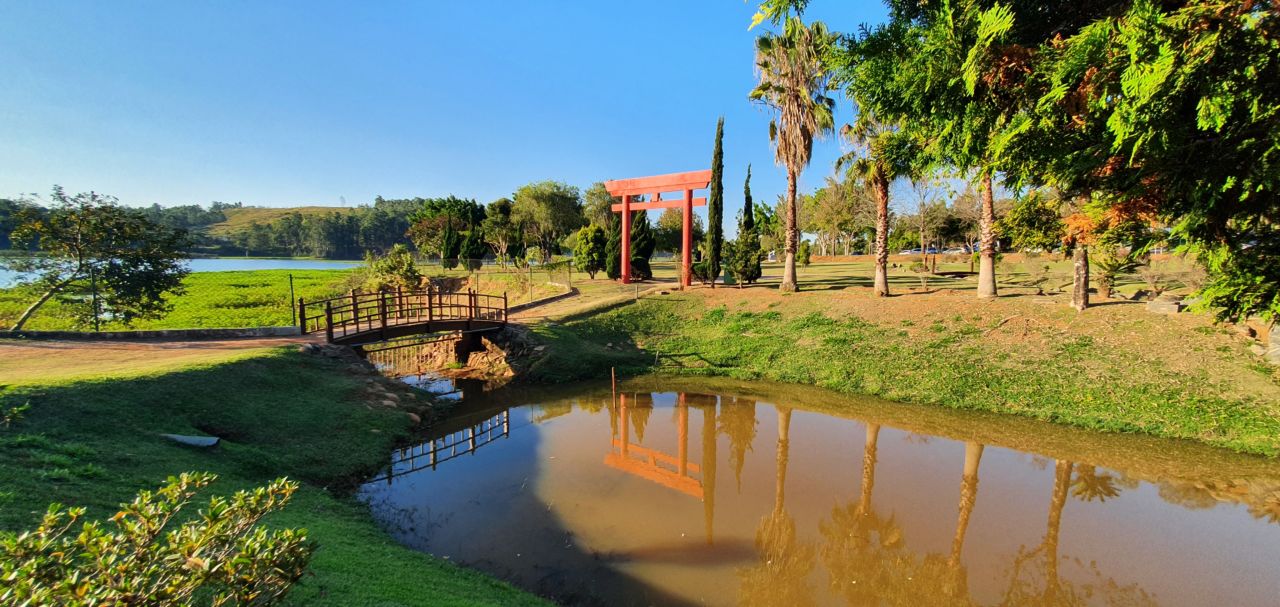 Parque com árvores, gramado, lagoa, ponte e totem vermelho japonês
