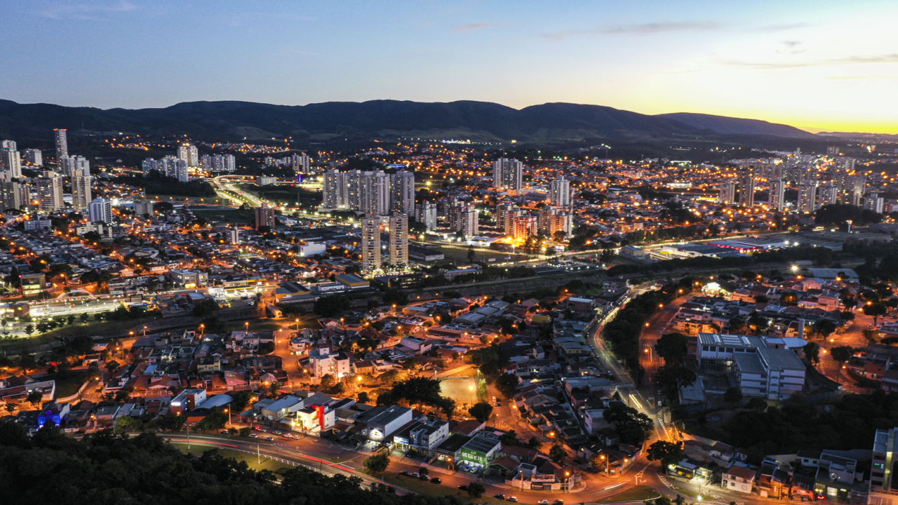Imagem aérea da cidade, com luzes acesas e serra ao fundo