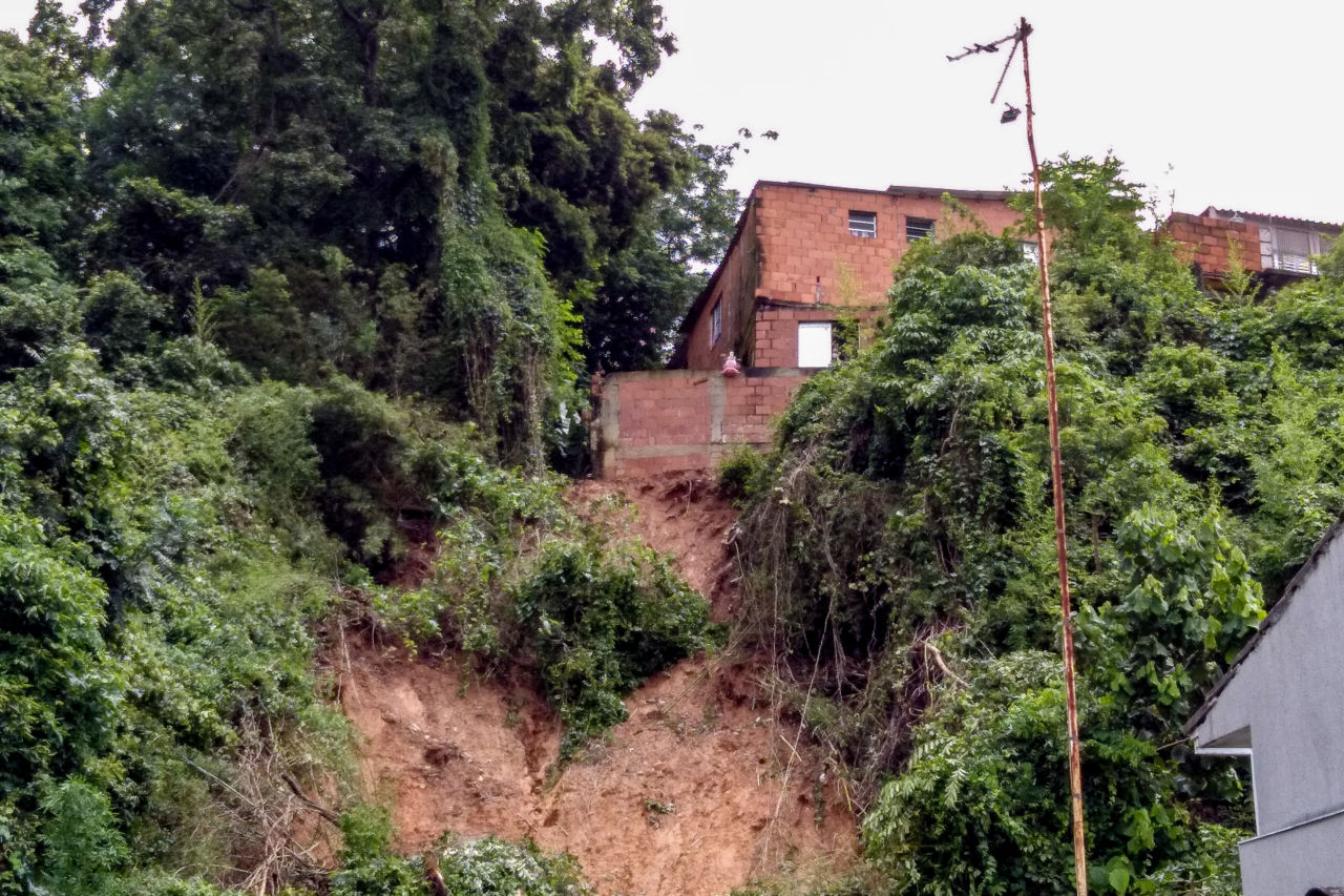 De baixo para cima, a área do morro em que ocorreu o deslizamento, com a casa acima e várias árvores e vegetação ao lado