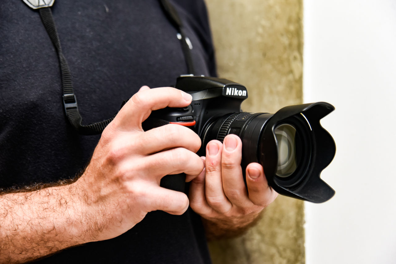 Detalhe de câmera fotográfica profissional sendo segurada por mãos e homem